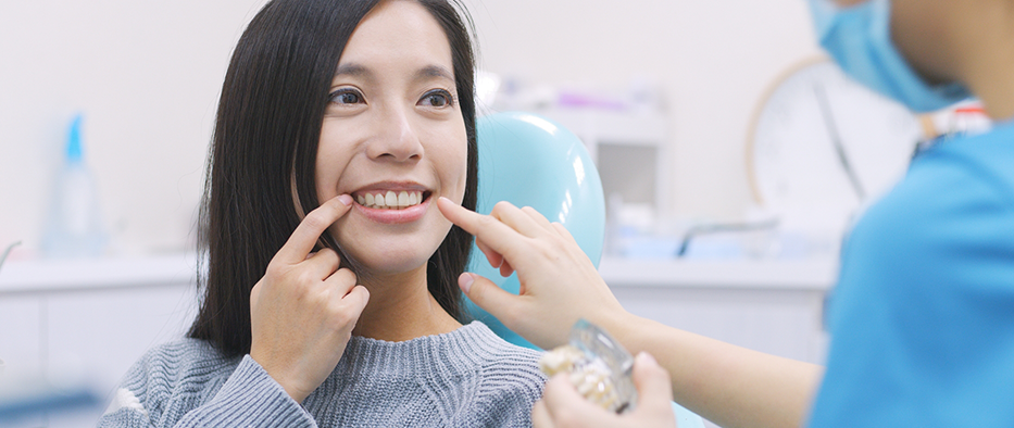 Woman in dental chair pointing to her smile